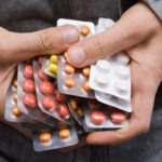 Unas manos sostienen muchos paquetes de diversas pastillas.