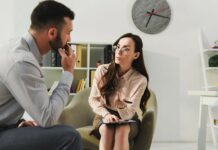 La psicoterapia puede prevenir las recaídas al dejar los antidepresivos Psicoterapeuta mujer, sentada en sillón con una libreta de notas y pluma en mano, inclinada hacía un hombre que se encuentra sentado de perfil, el hombre tiene la mano sobre su boca con expresión de escuchar de forma atenta.