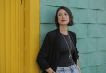 Estados Mórbidos, desgaste corporal en la vida contemporánea. Conversación con Dresda E. Méndez de la Brena (Parte 1) En la imagen se ve a Dresda Méndez, mujer con cabello negro lacio lo lleva a la altura bajo el mentón, tez blanca, vestida de negro, recargada en una pared color azul turquesa, a lado se encuentra una puerta color amarillo