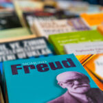 Se muestra la portada desenfocada de varios libros, sobre estos destaca uno cuyo portada de color azul muestra en grande el nombre de Freud